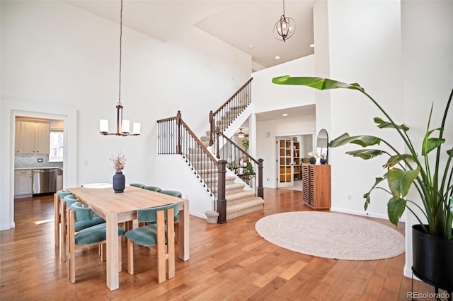 dining room with an inviting chandelier, baseboards, light wood-style floors, a high ceiling, and stairway