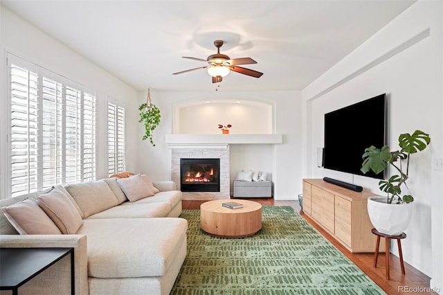 living room featuring a glass covered fireplace, ceiling fan, and wood finished floors