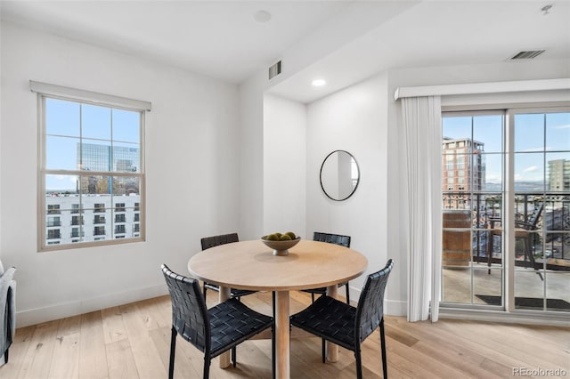 dining area with light wood-style floors, baseboards, visible vents, and a city view