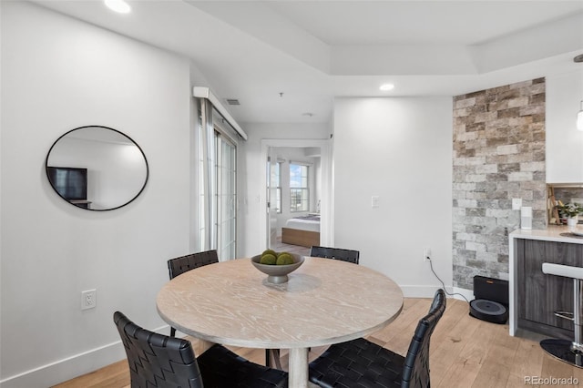 dining space with recessed lighting, light wood-type flooring, a raised ceiling, and baseboards