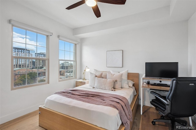 bedroom featuring a ceiling fan, a city view, light wood-style flooring, and baseboards