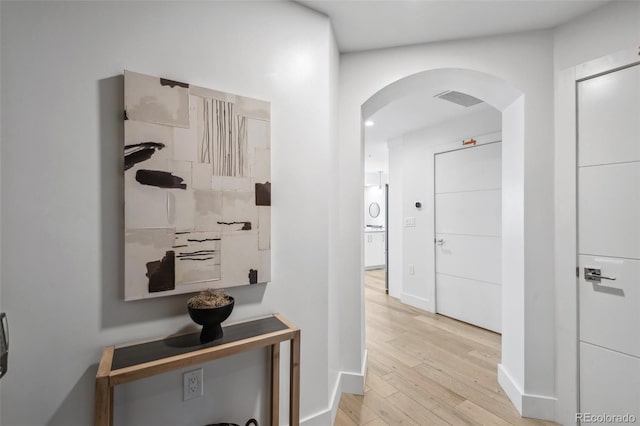 corridor with baseboards, visible vents, arched walkways, and wood finished floors