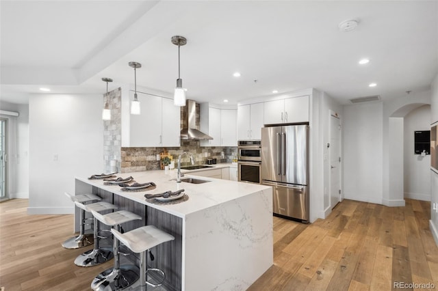 kitchen with arched walkways, stainless steel appliances, a peninsula, wall chimney exhaust hood, and tasteful backsplash