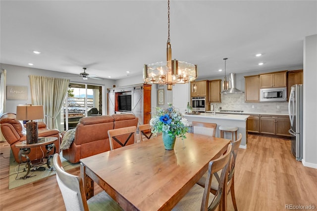 dining space featuring ceiling fan, a barn door, sink, and light wood-type flooring