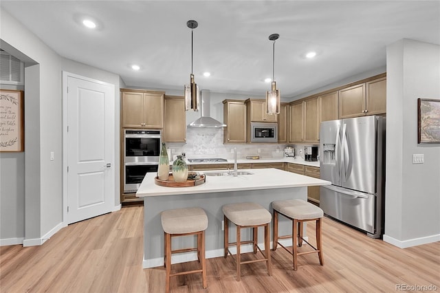 kitchen featuring pendant lighting, a breakfast bar area, a kitchen island with sink, stainless steel appliances, and wall chimney exhaust hood