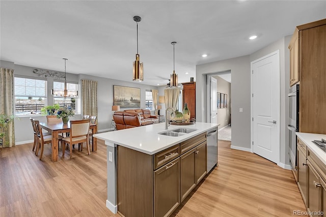 kitchen featuring decorative light fixtures, an island with sink, sink, stainless steel appliances, and light wood-type flooring