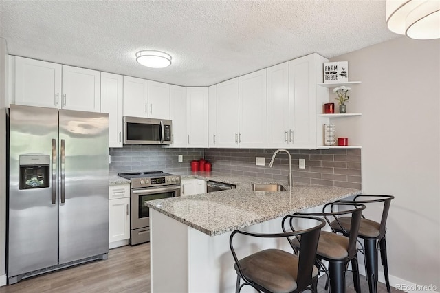 3465 S Poplar St Unit 305, Denver, CO 80224 - kitchen featuring appliances with stainless steel finishes, open shelves, a peninsula, a sink, and white cabinets