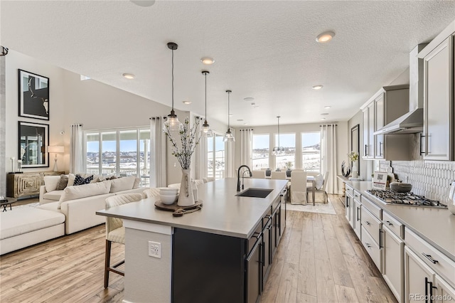 kitchen with sink, light hardwood / wood-style flooring, hanging light fixtures, stainless steel gas stovetop, and an island with sink