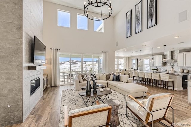 living room with a tiled fireplace, a healthy amount of sunlight, a high ceiling, and light wood-type flooring