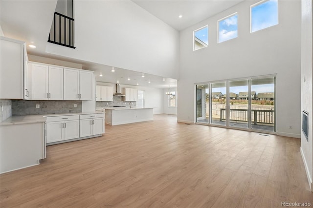 16537 Black Rose Cir, Parker, CO 80134 - kitchen with wall chimney range hood, open floor plan, white cabinetry, and light wood-type flooring