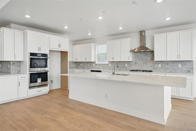 16537 Black Rose Cir, Parker, CO 80134 - kitchen featuring white cabinets, a center island with sink, double oven, wall chimney range hood, and gas stovetop