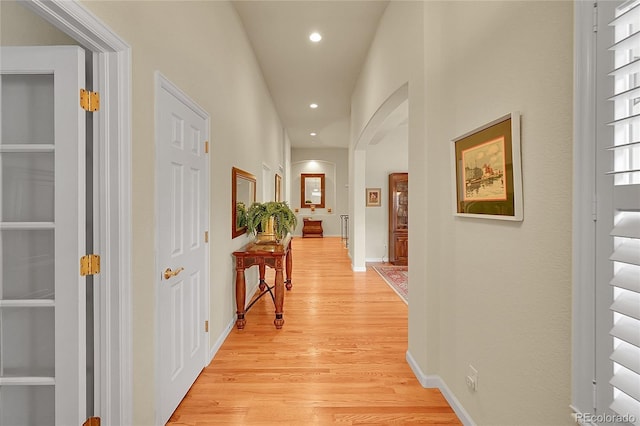 corridor with light wood-type flooring, arched walkways, baseboards, and recessed lighting