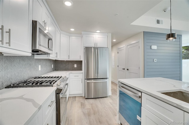 kitchen with light wood-type flooring, stainless steel appliances, white cabinets, decorative light fixtures, and backsplash