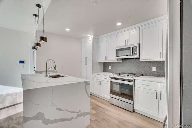 kitchen with stainless steel appliances, light wood-type flooring, pendant lighting, sink, and white cabinetry