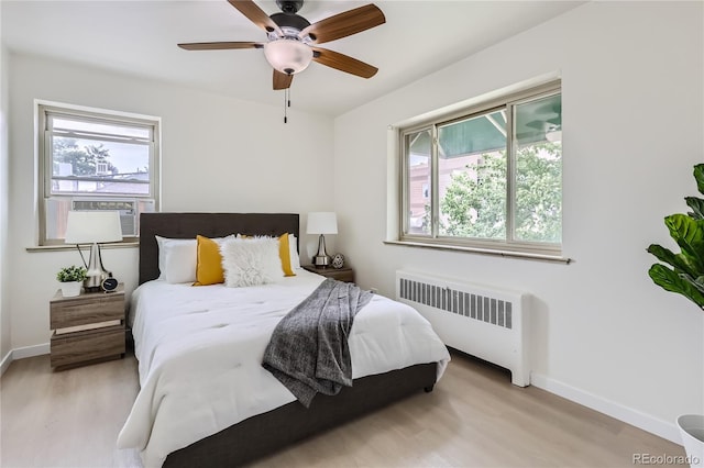 bedroom with baseboards, multiple windows, radiator heating unit, and light wood finished floors