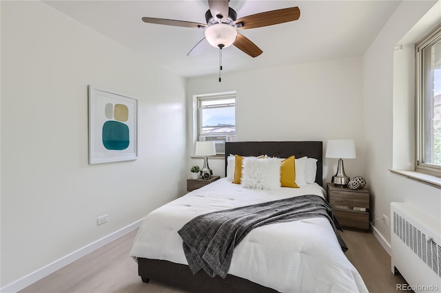 bedroom featuring light wood finished floors, ceiling fan, radiator heating unit, and baseboards