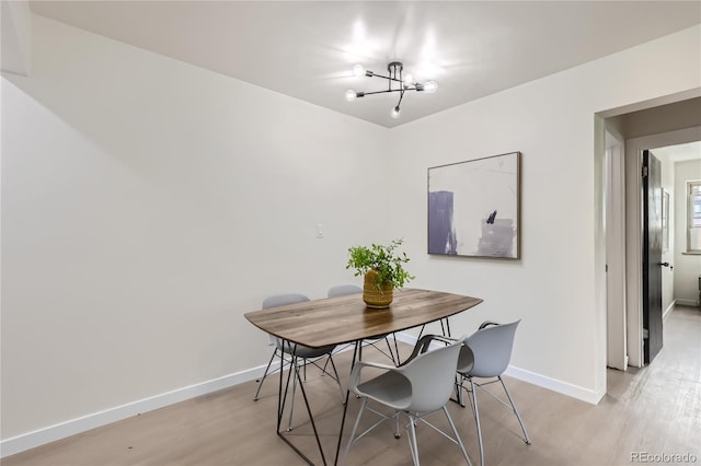 dining room with light wood-style flooring, a notable chandelier, and baseboards