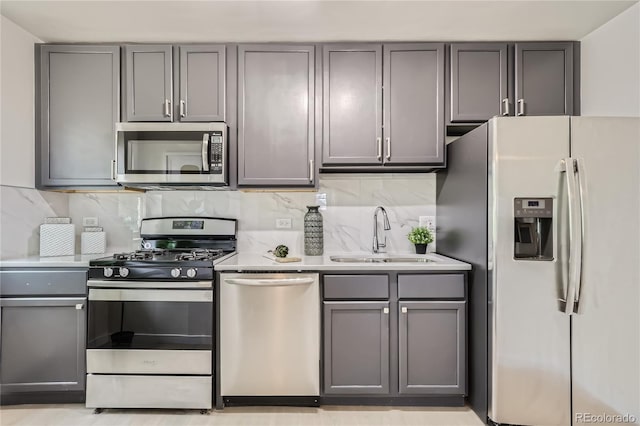 kitchen featuring gray cabinetry, a sink, backsplash, stainless steel appliances, and light countertops