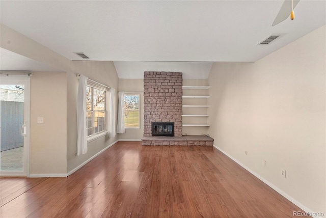 unfurnished living room featuring hardwood / wood-style flooring, ceiling fan, a healthy amount of sunlight, and a stone fireplace