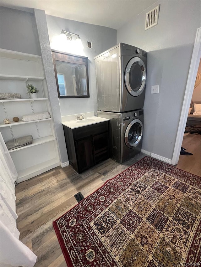 clothes washing area featuring wood-type flooring and stacked washing maching and dryer