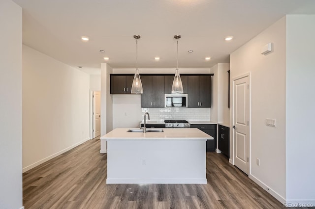 kitchen with stove, decorative light fixtures, a kitchen island with sink, light countertops, and a sink