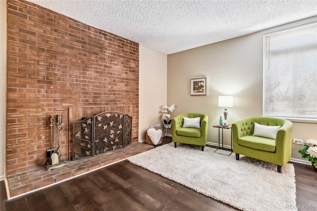 living area with a textured ceiling, a brick fireplace, wood finished floors, and baseboards