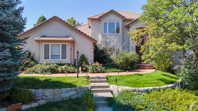 rear view of property with a yard, a tile roof, and stucco siding