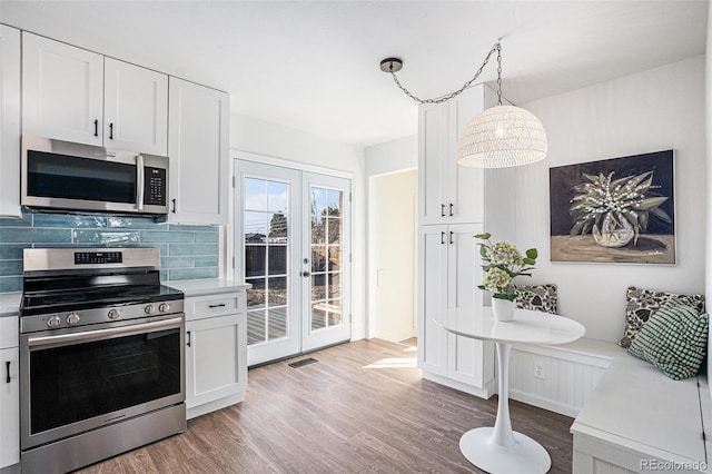 kitchen with white cabinets, decorative light fixtures, backsplash, and stainless steel appliances