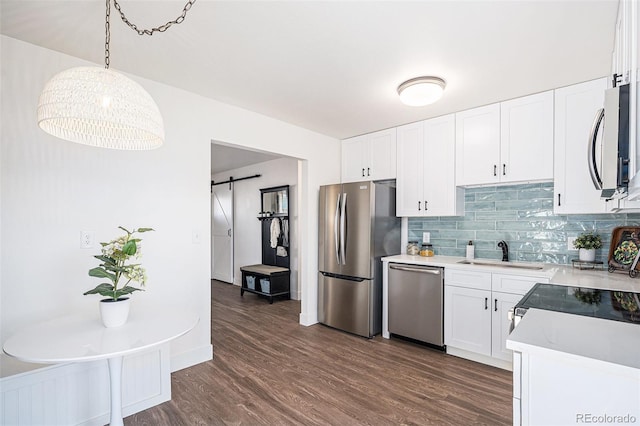 kitchen with sink, hanging light fixtures, a barn door, appliances with stainless steel finishes, and white cabinetry