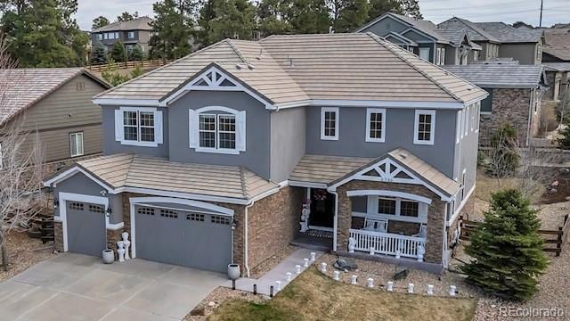 view of front of property featuring driveway, stone siding, covered porch, a garage, and stucco siding