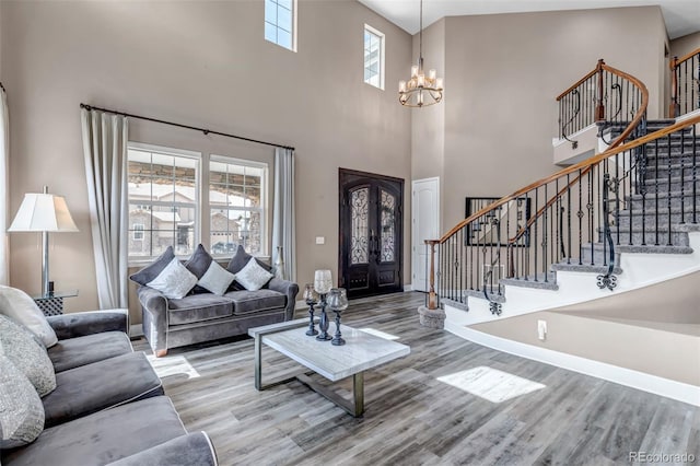 living area featuring a towering ceiling, baseboards, an inviting chandelier, wood finished floors, and stairway