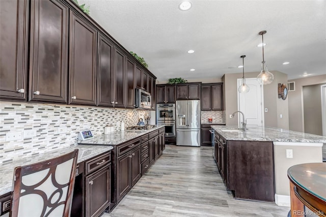 kitchen featuring a center island with sink, dark brown cabinetry, stainless steel appliances, and a sink