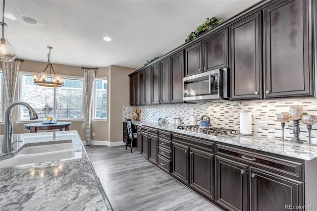 kitchen with a sink, decorative backsplash, stainless steel appliances, light wood finished floors, and baseboards