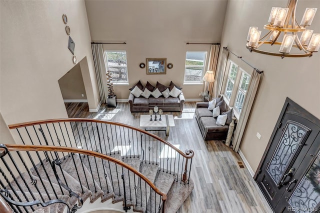 staircase with wood finished floors, a high ceiling, a notable chandelier, and a healthy amount of sunlight