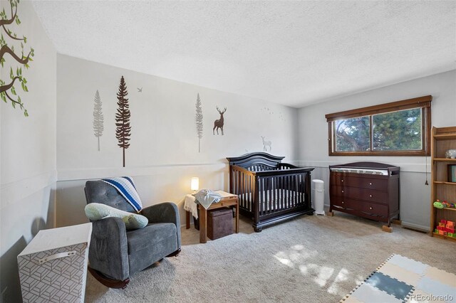 bedroom featuring a crib, a textured ceiling, and light colored carpet