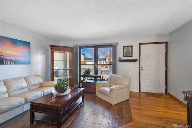 living room with dark wood-style flooring, a textured ceiling, and baseboards