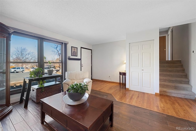 living area featuring a textured ceiling, stairway, wood finished floors, and baseboards