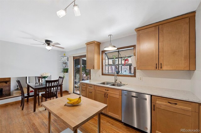 kitchen with light wood-style flooring, hanging light fixtures, light countertops, stainless steel dishwasher, and a sink