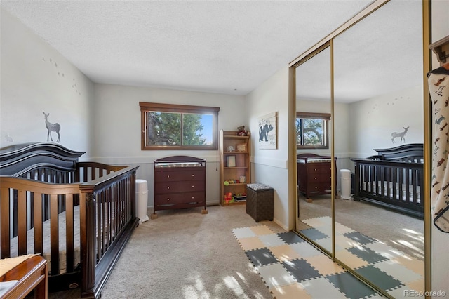 bedroom featuring a textured ceiling, a closet, a nursery area, and light colored carpet