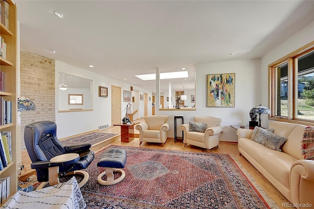 living room featuring recessed lighting, brick wall, a skylight, visible vents, and light wood-style floors