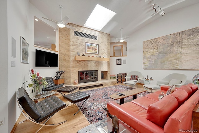 living room with a ceiling fan, a skylight, a fireplace, and wood finished floors