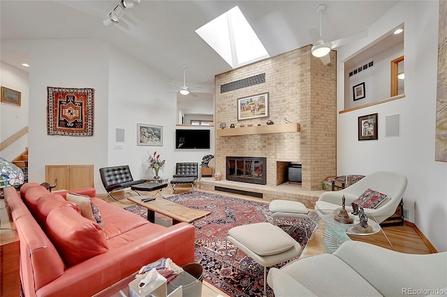 living area featuring high vaulted ceiling, a skylight, a fireplace, and a ceiling fan