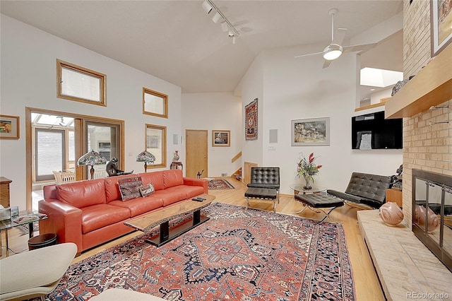 living area with high vaulted ceiling, a brick fireplace, stairway, and wood finished floors