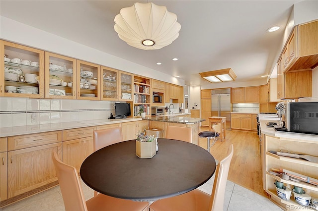 kitchen featuring built in appliances, a sink, glass insert cabinets, and light brown cabinets