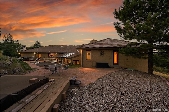 back of house at dusk featuring a patio area, a tile roof, and a chimney