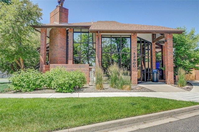 2181 S Troy Way Unit 103, Aurora, CO 80014 - view of front of property featuring brick siding, a chimney, a front lawn, and a shingled roof