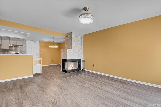 2181 S Troy Way Unit 103, Aurora, CO 80014 - unfurnished living room featuring light wood-style flooring, a multi sided fireplace, and a raised ceiling