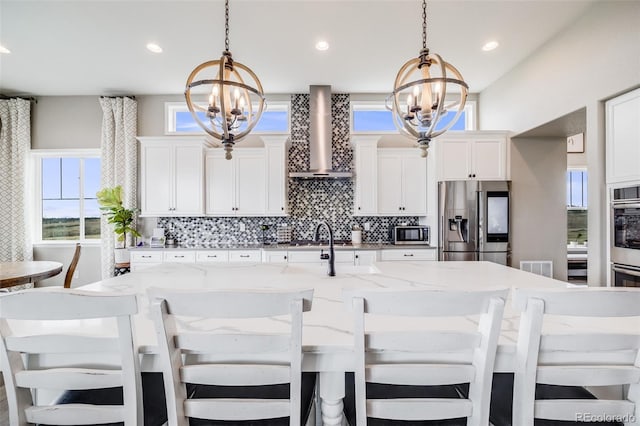 8750 Red Primrose St, Franktown, CO 80116 - kitchen featuring an inviting chandelier, wall chimney exhaust hood, tasteful backsplash, appliances with stainless steel finishes, and hanging light fixtures