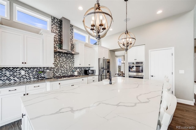 8750 Red Primrose St, Franktown, CO 80116 - kitchen with decorative backsplash, wall chimney range hood, a chandelier, a large island with sink, and stainless steel appliances
