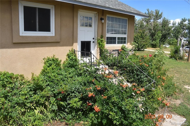 property entrance with roof with shingles and stucco siding